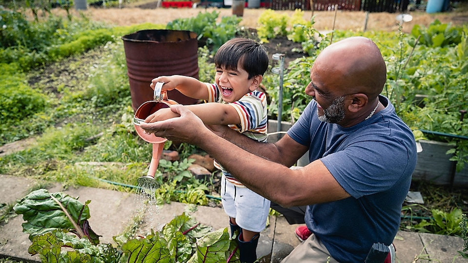 Egy férfi egy mosolygó gyereknek segít a növények öntözésében a kertben