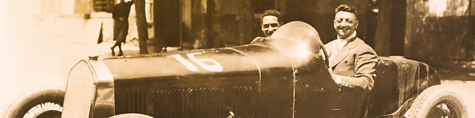 Enzo Ferrari fekete-fehér fényképe, ahogy az első Ferrarik egyikében ül.