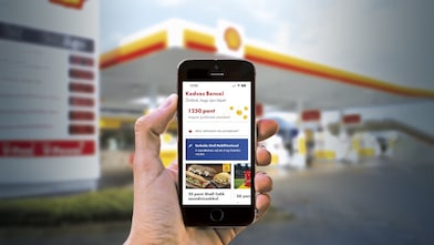 Kézben tartott mobiltelefon egy Shell töltőállomás előtt