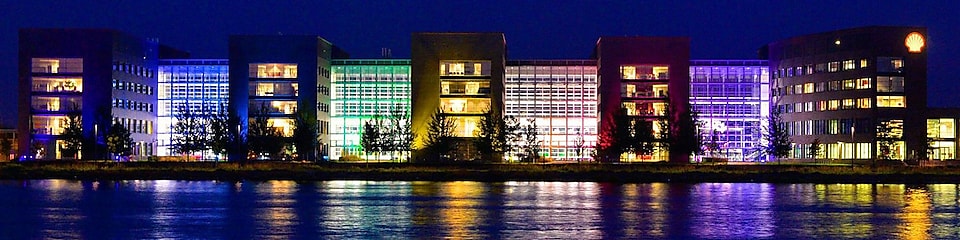 Kivilágított irodaépületek csoportja, amelynek képe éjszaka visszatükröződik a vízben