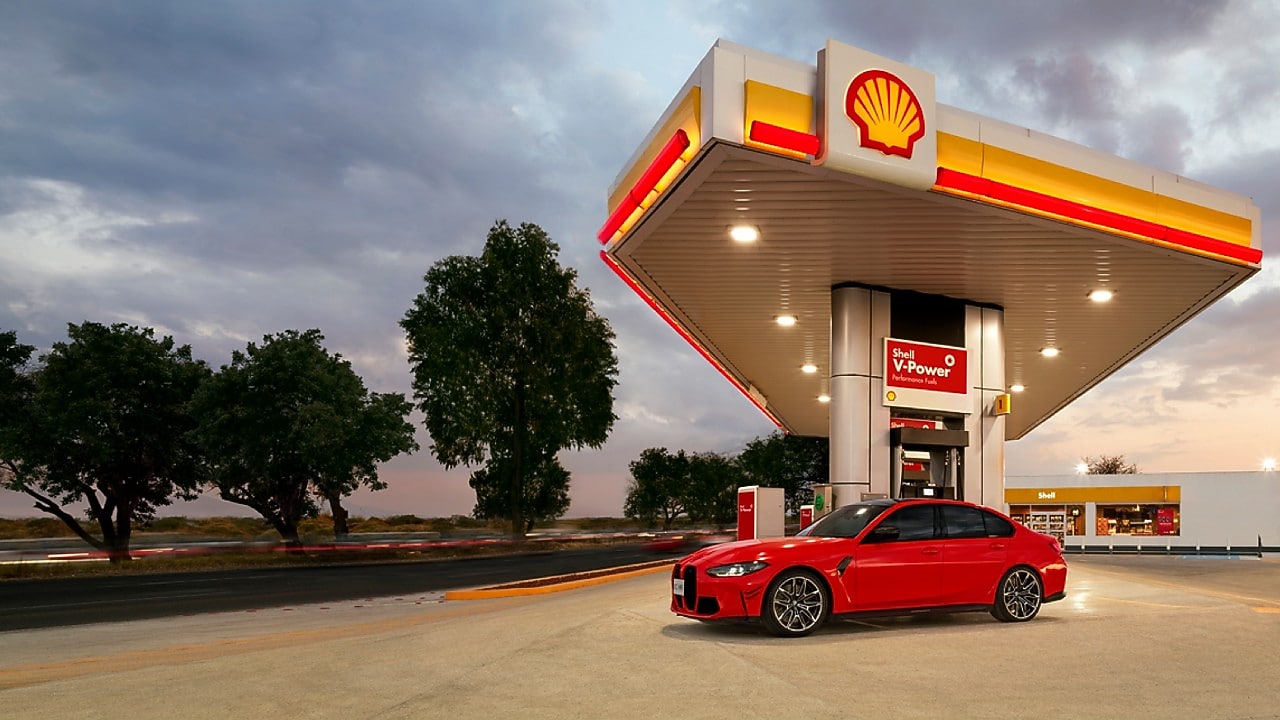 A képen bal oldalán egy mosolygó nőt látunk, a háttérben pedig egy hegyekbe tartó autópályát esti fényekben. A kép közepén pedig a Shell V-Power Diesel logo található.