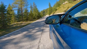 kék autó suhan fenyőfákkal övezett hegyi úton