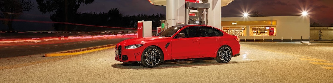 A képen bal oldalán egy mosolygó nőt látunk, a háttérben pedig egy hegyekbe tartó autópályát esti fényekben. A kép közepén pedig a Shell V-Power Diesel logo található.