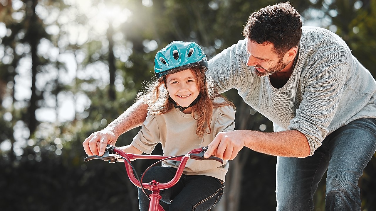 Egy mosolygós kislány kerékpározni tanul apukája segítségével