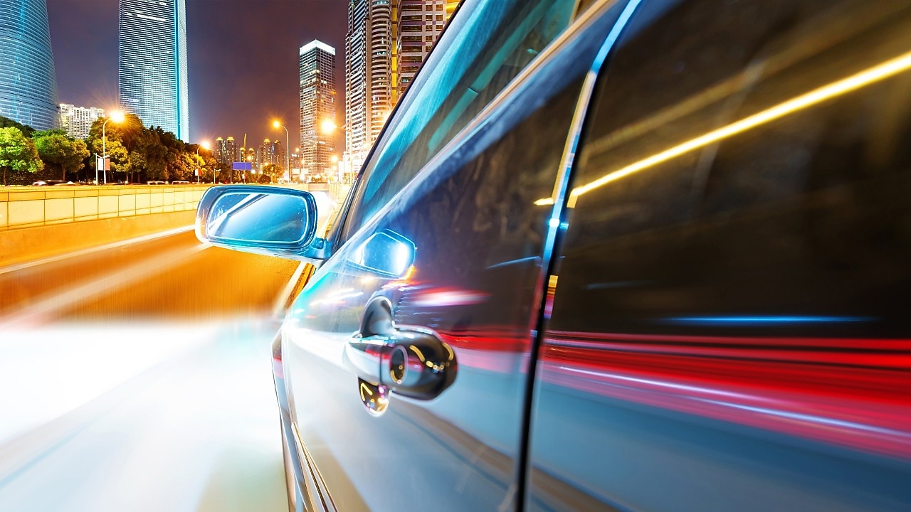 Egy autó halad az éjszakában egy városi úton, elmosódott fénycsíkokkal a háttérben, ami a sebességet jelzi.