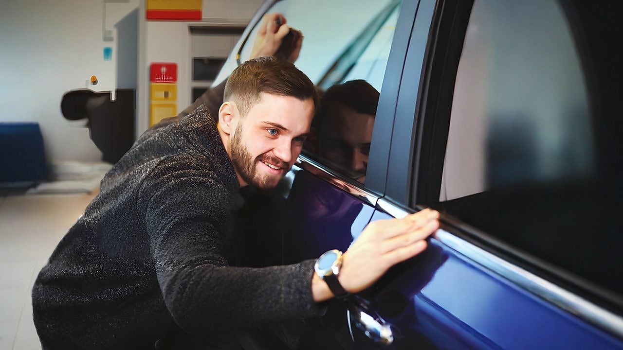 A képen egy férfi, amint megcsodálja autója tisztaságát.