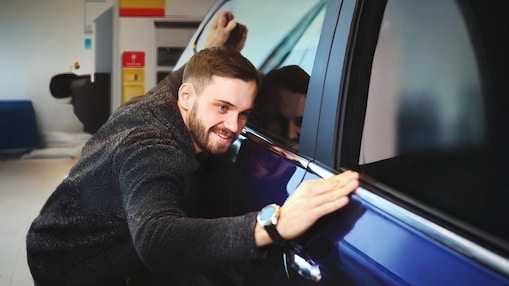 A képen egy férfi, amint megcsodálja autója tisztaságát.