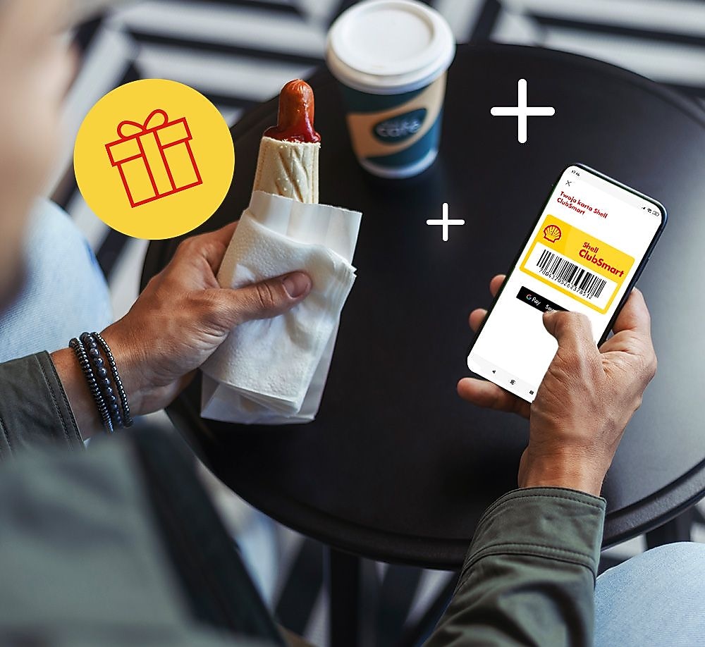 A person holding a phone and a hot dog