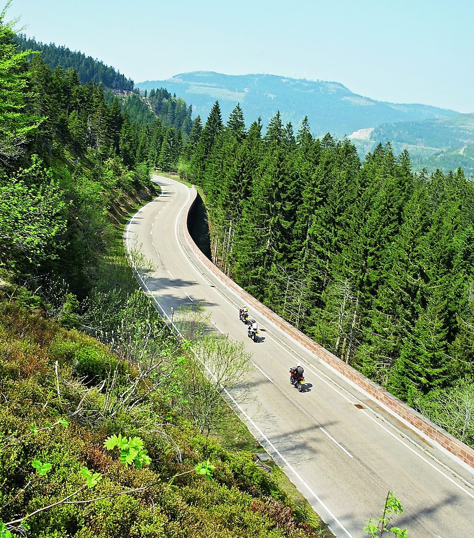 Három motorkerékpár versenyez egy fákkal szegélyezett hegyi úton