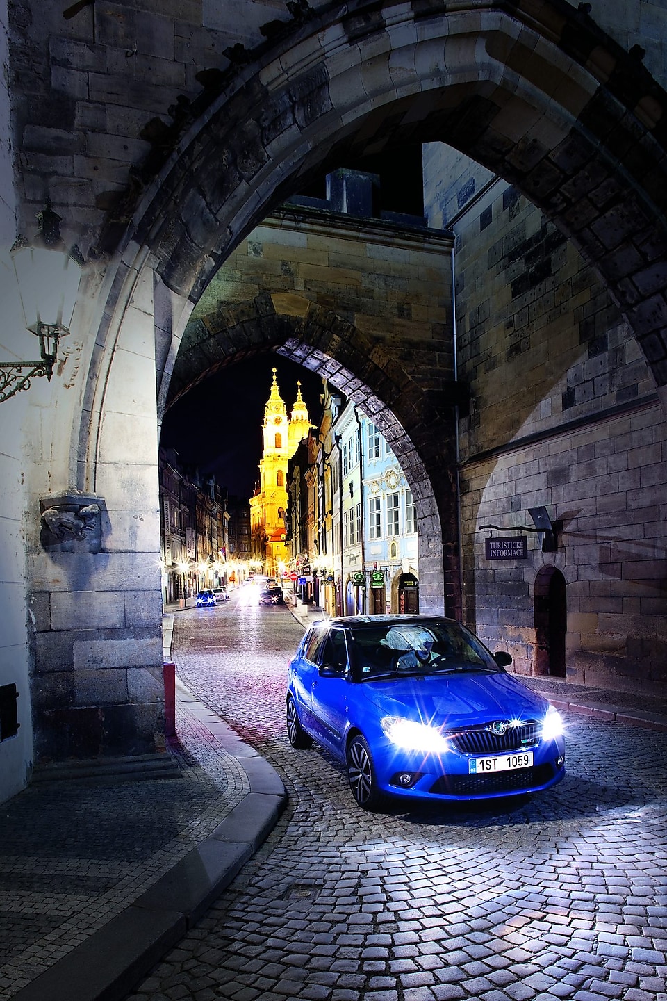 Kék autó parkol egy árkád alatt a macskaköves prágai úton az éjszakában
