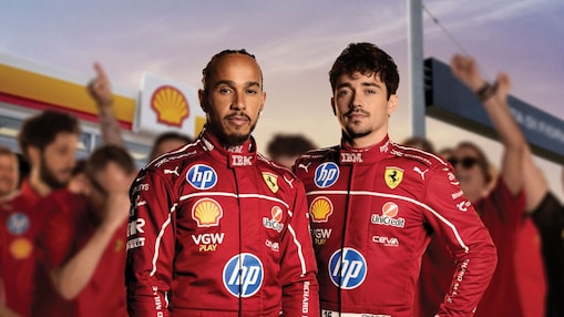 Lewis Hamilton és Charles Leclerc egy Shell töltőállomás előtt áll mögöttük pedig szurkolók örülnek